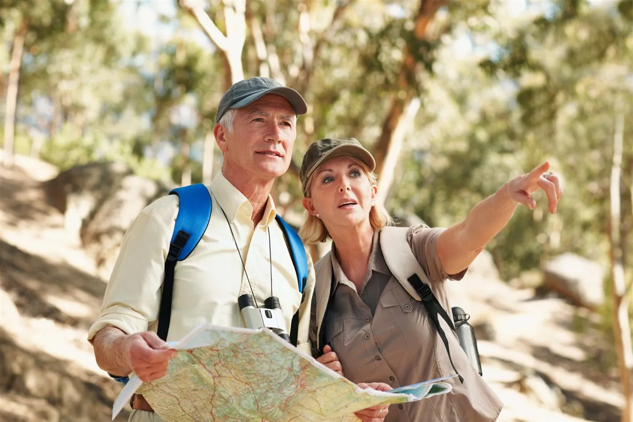 An older couple outdoors reading a map together, one pointing toward the trail ahead